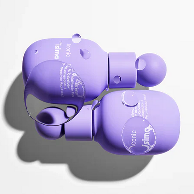 Two purple bottles of the Isima Iconic Scalp System with rounded caps lie side by side on a white surface, featuring white text and water droplets. Designed for effective scalp care, these bottles cast soft shadows and subtle reflections.