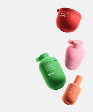 Four colorful Isima hair care product bottles are arranged diagonally on a white background; red, green, pink, and orange bottles with minimalist labels and rounded shapes.