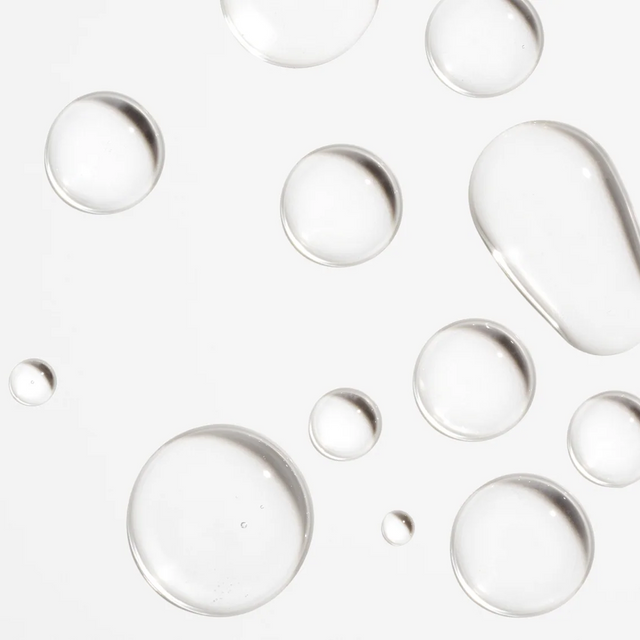 Crystal-clear droplets of the Iconic Scalp System by Isima are artfully scattered across a white background, forming a minimal and clean pattern that captures the refreshing simplicity of effective scalp care—ideal for anyone seeking visible hair growth results in just 90 days.