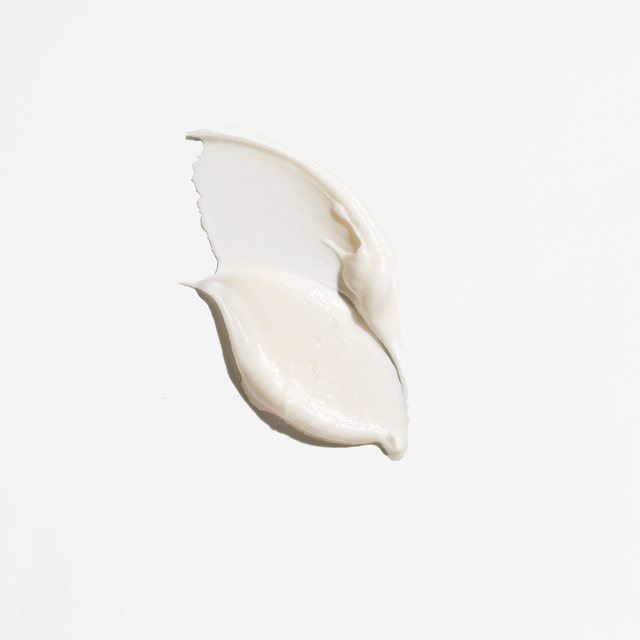 A swipe of creamy white lotion from isima’s Shakira’s Súperbomba Set, reminiscent of a nourishing peptide mask, is spread on a plain white background.