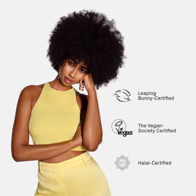 A woman in a yellow sleeveless outfit stands beside icons and text for Leaping Bunny, Vegan Society, and Halal certifications, highlighting the ethical and dietary approvals of isima’s Shakira’s Wash + Care Kit ($144 value). She represents confidence inspired by this expertly formulated kit for enhanced strength and healthy-looking hair.